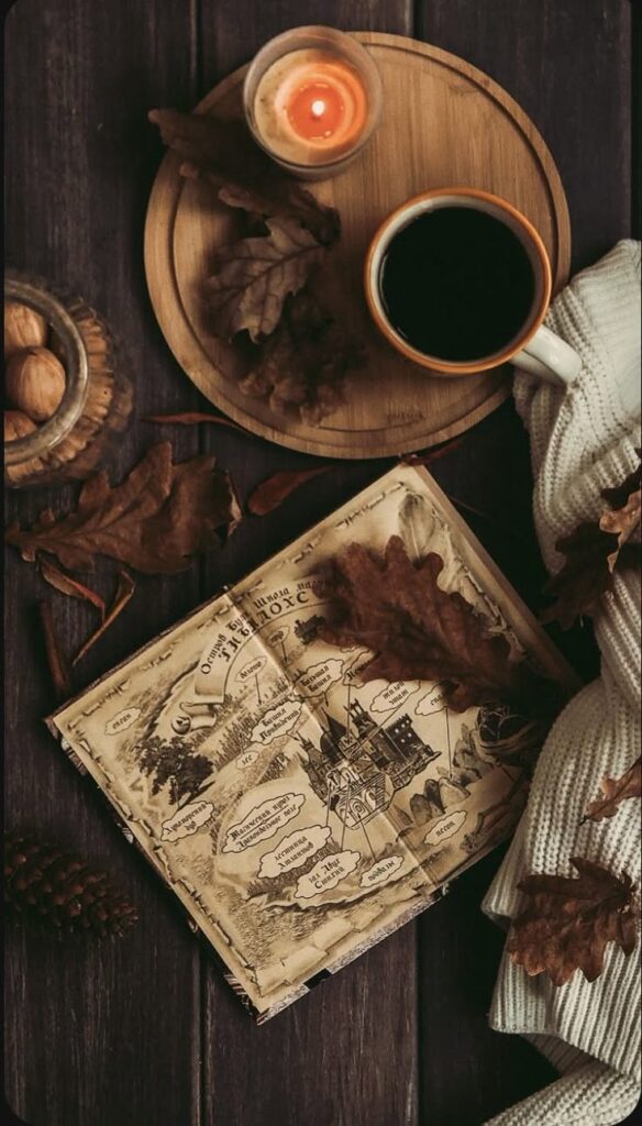 Cozy autumn scene with coffee, candle, vintage map, and fall leaves on wooden table. Warm and inviting fall atmosphere.