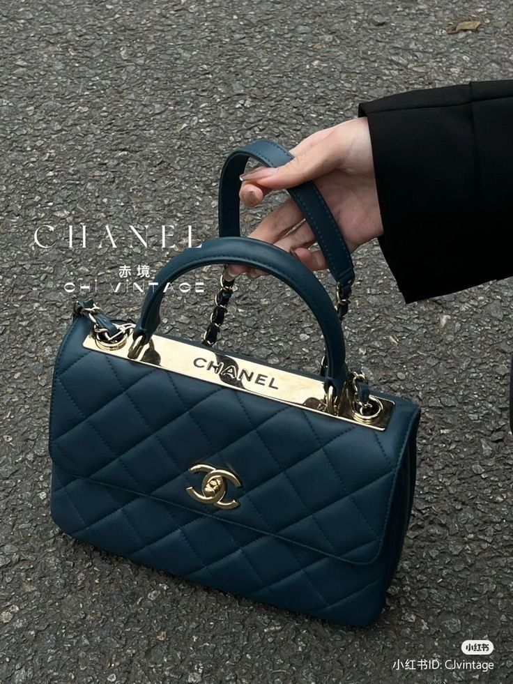 Luxury blue quilted handbag with Chanel logo, gold accents, and chain strap, held by a hand on gray pavement.