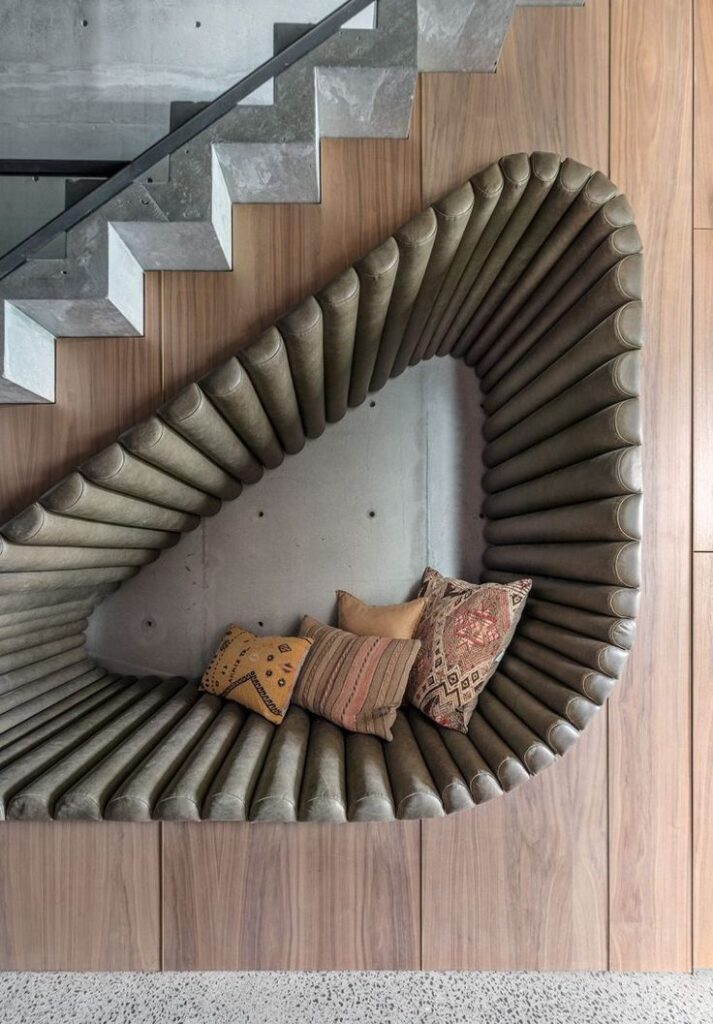 Modern staircase with a unique triangular nook, cushioned seating, and decorative pillows for a cozy reading area.