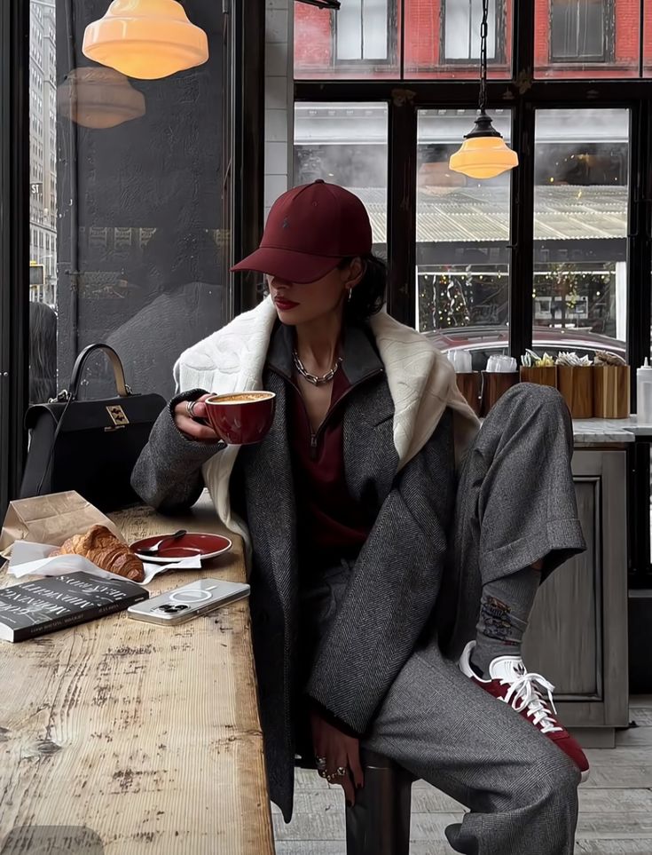 Screenshot Fashionable woman in cafe sipping coffee, wearing stylish gray coat and red cap, with croissant on wooden table. | Sky Rye Design Fashionable woman in cafe sipping coffee, wearing stylish gray coat and red cap, with croissant on wooden table.