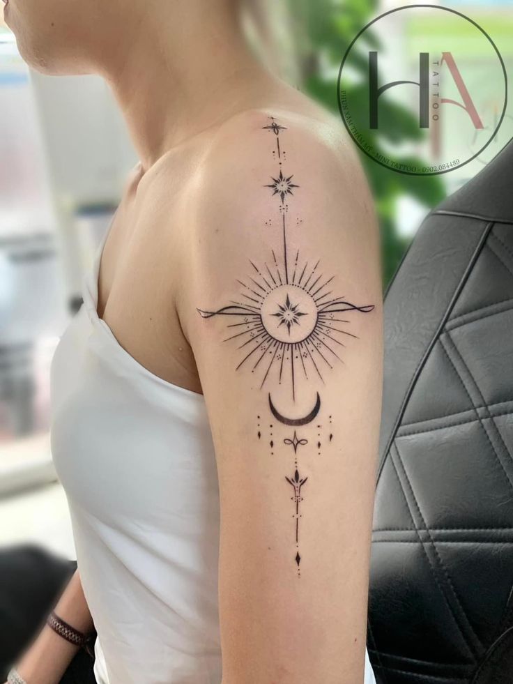 Abstract celestial tattoo design on upper arm featuring sun, stars, and moon elements in black ink.