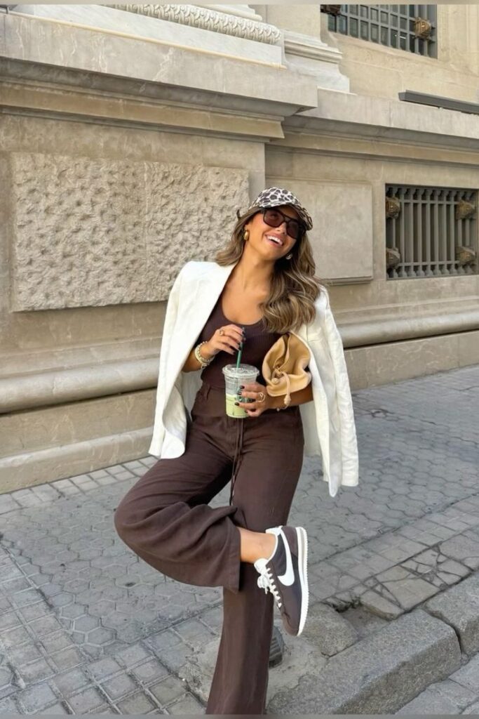 Fashion-forward woman in stylish outfit, enjoying a drink and smiling on an urban street, embodying casual chic vibes.
