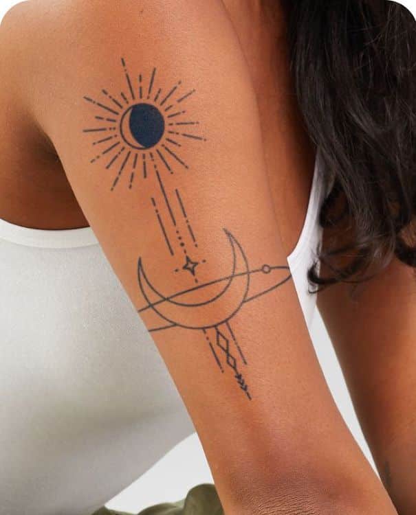 Minimalist arm tattoo featuring crescent moon and sun design against a sleeveless white top background.