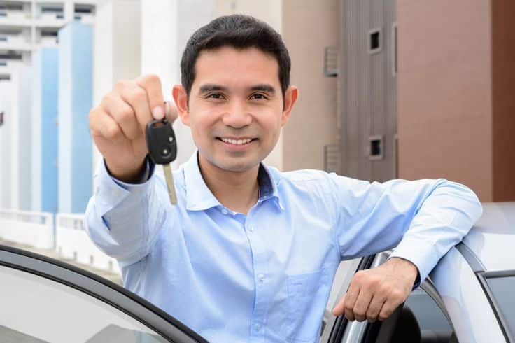 Smiling man holding a car key while standing by his vehicle.