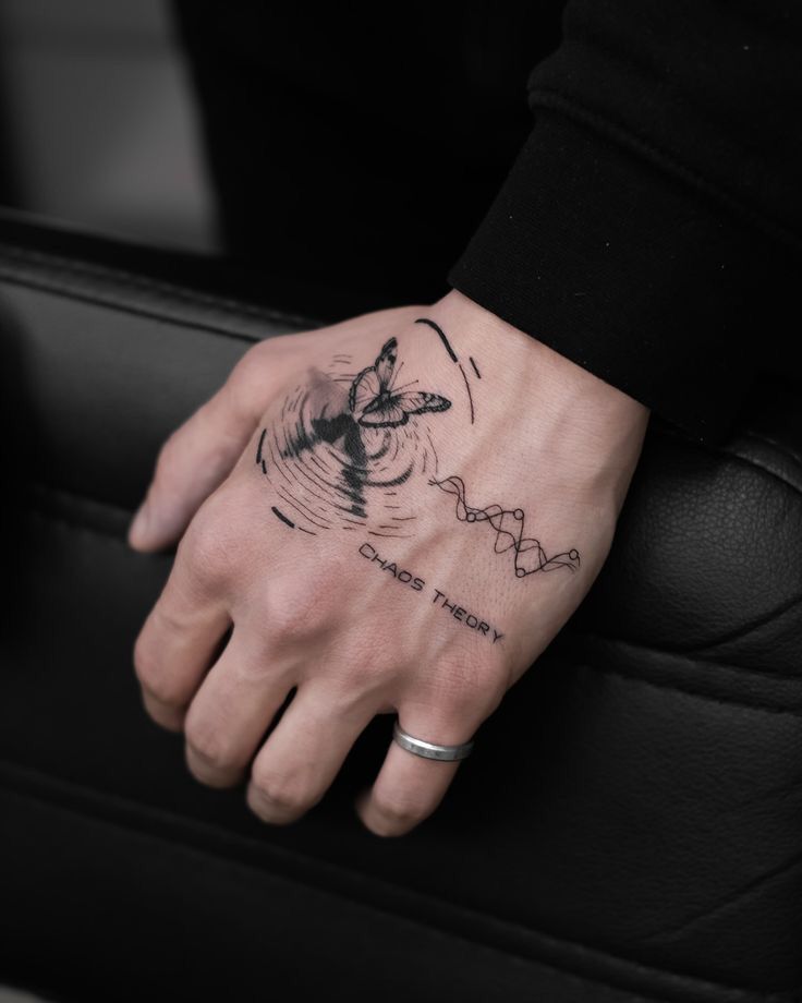 Tattoo of butterfly and wave pattern with Chaos Theory text on hand, wearing a silver ring.