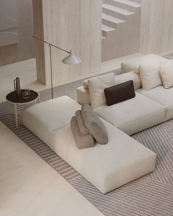 Modern minimalist living room with beige sectional sofa, layered cushions, floor lamp, and round side table.