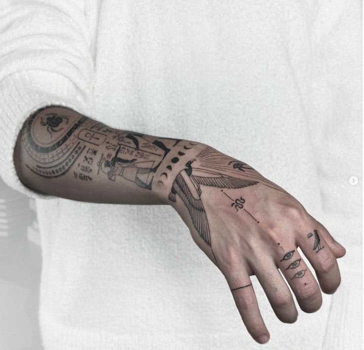Abstract tattoo arm art featuring geometric and symbolic designs in black ink on a person wearing a white long-sleeve shirt.
