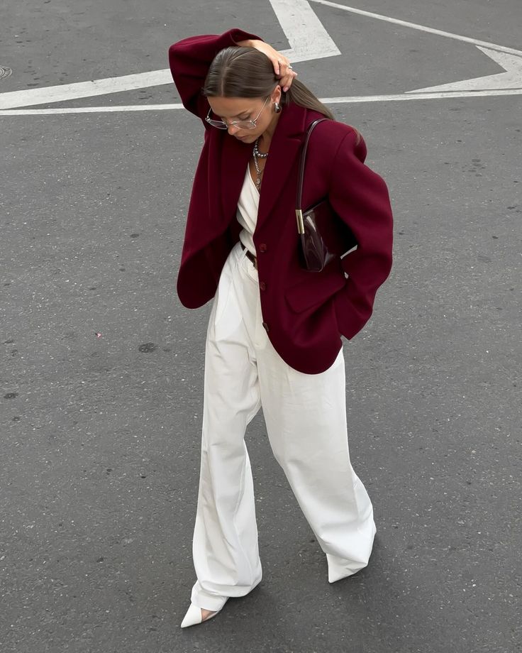 Fashionable woman in burgundy blazer and white pants walking on street, stylish and chic urban outfit.