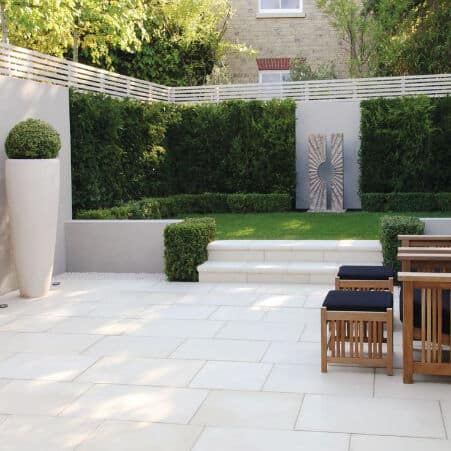 Contemporary patio with wooden furniture and greenery, featuring manicured hedges and decorative elements in a serene garden.