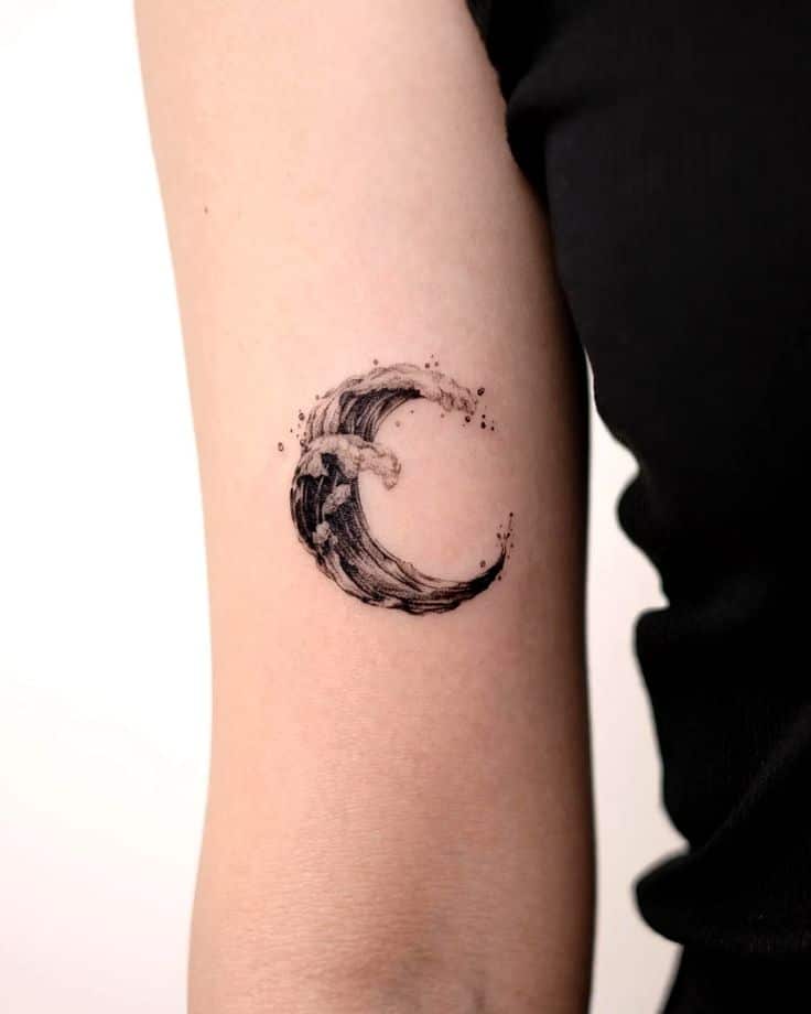 Minimalist crescent moon tattoo design on upper arm, featuring detailed wave art in black ink.