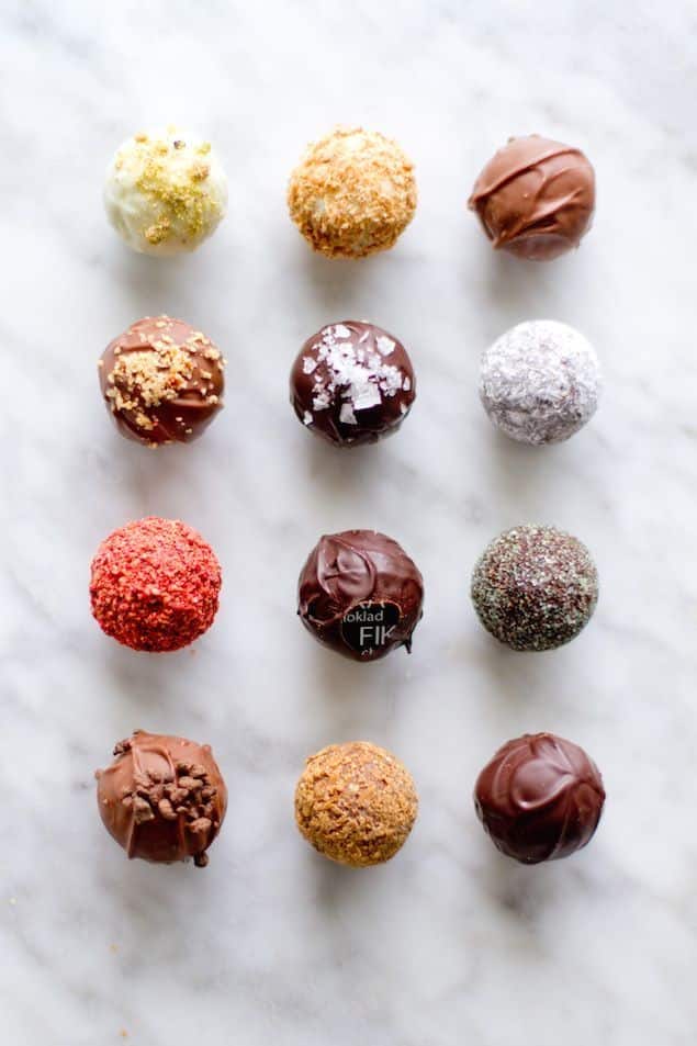 Assorted gourmet chocolate truffles arranged in a grid on a marble surface, showcasing various toppings and flavors.