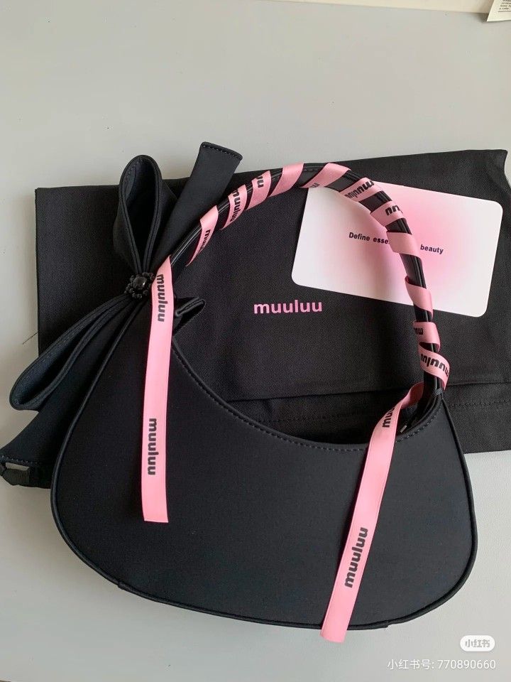 Black handbag with pink handle and ribbons, featuring muuluu branding on a gray surface.