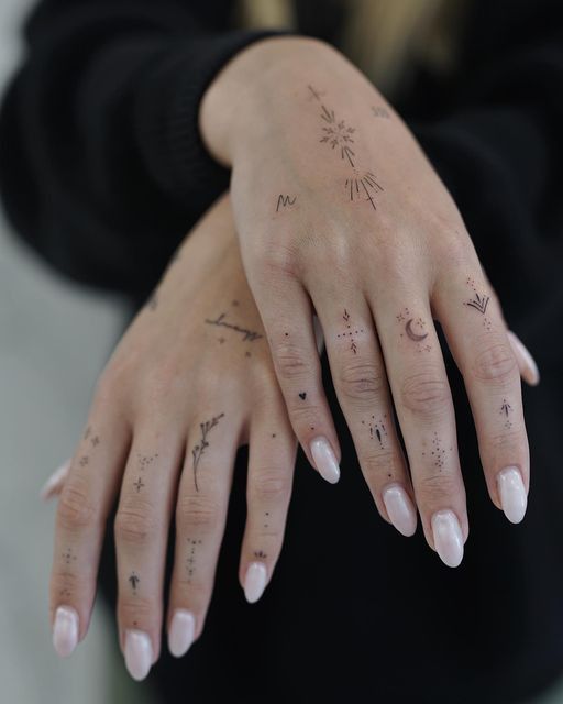 Delicate hand tattoos with symbols and designs on fingers and hands, showcasing minimalist body art style.