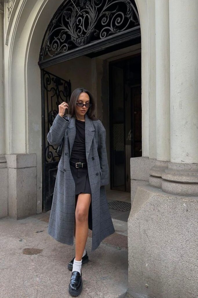Woman in stylish plaid coat and sunglasses poses outside ornate building.