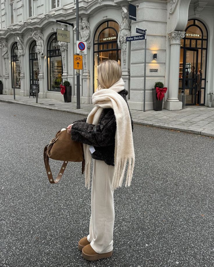 Woman in cozy winter outfit, standing in urban street with shops and signage in the background.