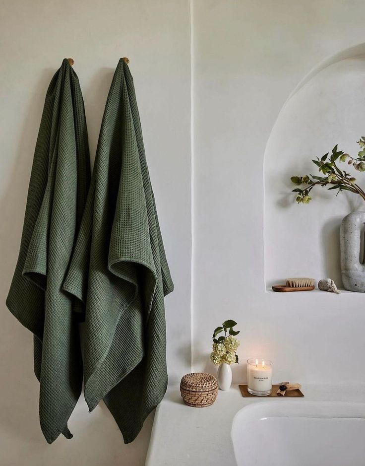 Green towels hanging in a minimalist bathroom with a lit candle and decorative elements on a white surface.