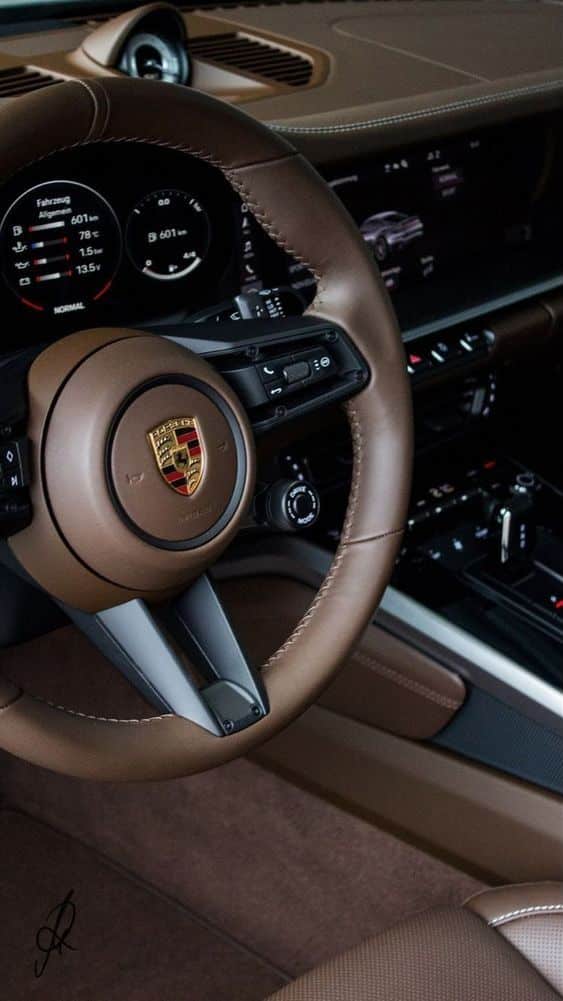 Luxury car interior with brown leather steering wheel, dashboard, and digital displays in a modern vehicle.