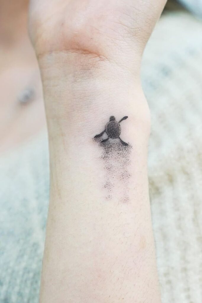 Minimalist watercolor turtle tattoo on inner wrist, showcasing delicate dot work and subtle shading for a unique design.
