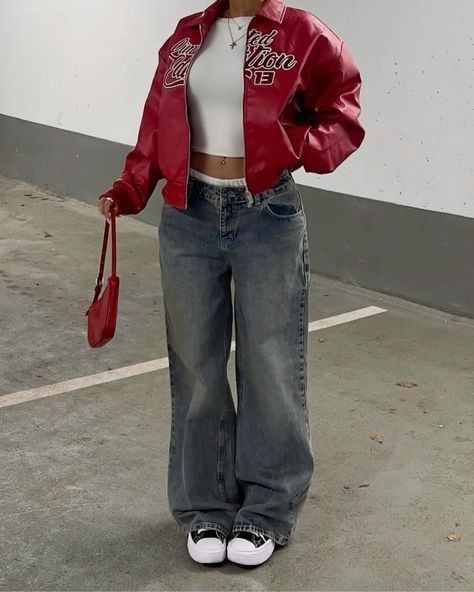 Woman in red jacket and baggy jeans, holding a red purse in a parking garage.