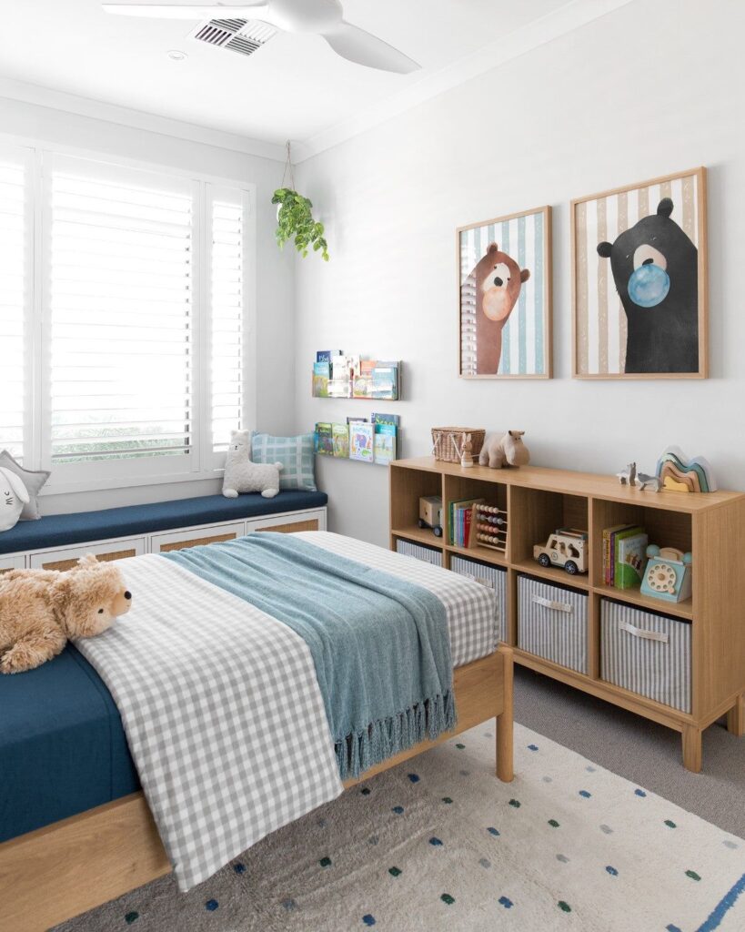 Child's room with a cozy bed, wooden shelves, playful bear art, and a furry toy on a blue checkered blanket.
