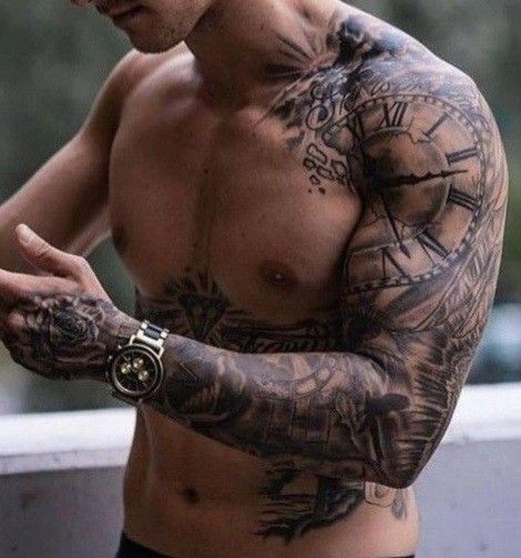 Tattooed man displaying intricate sleeve with clock design, wearing a watch and standing shirtless outdoors.