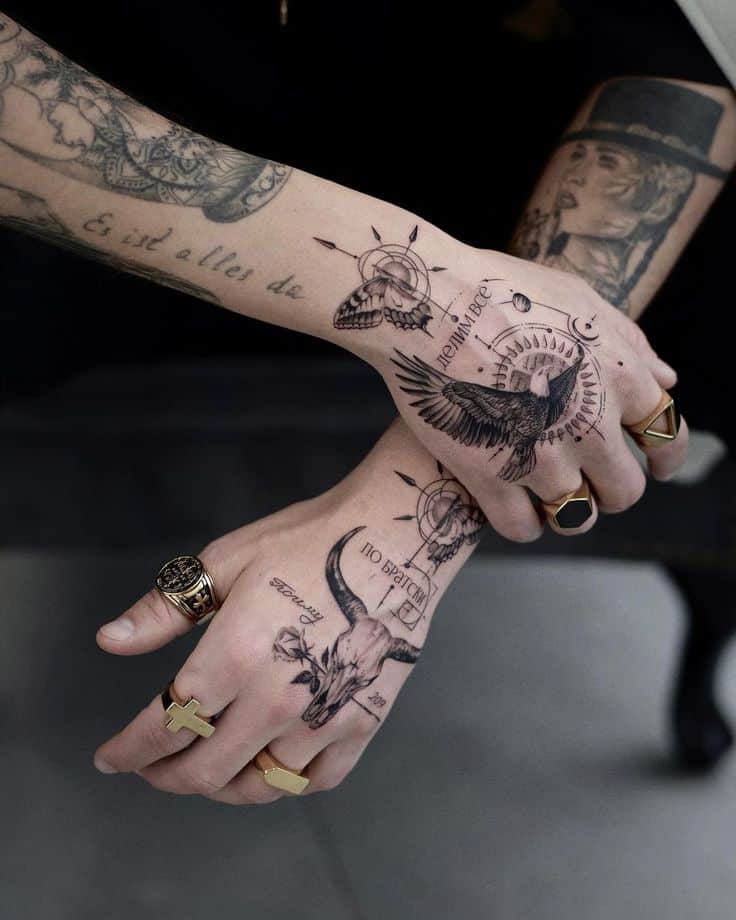Tattooed hands with intricate designs, rings, and detailed artwork featuring birds and skulls.
