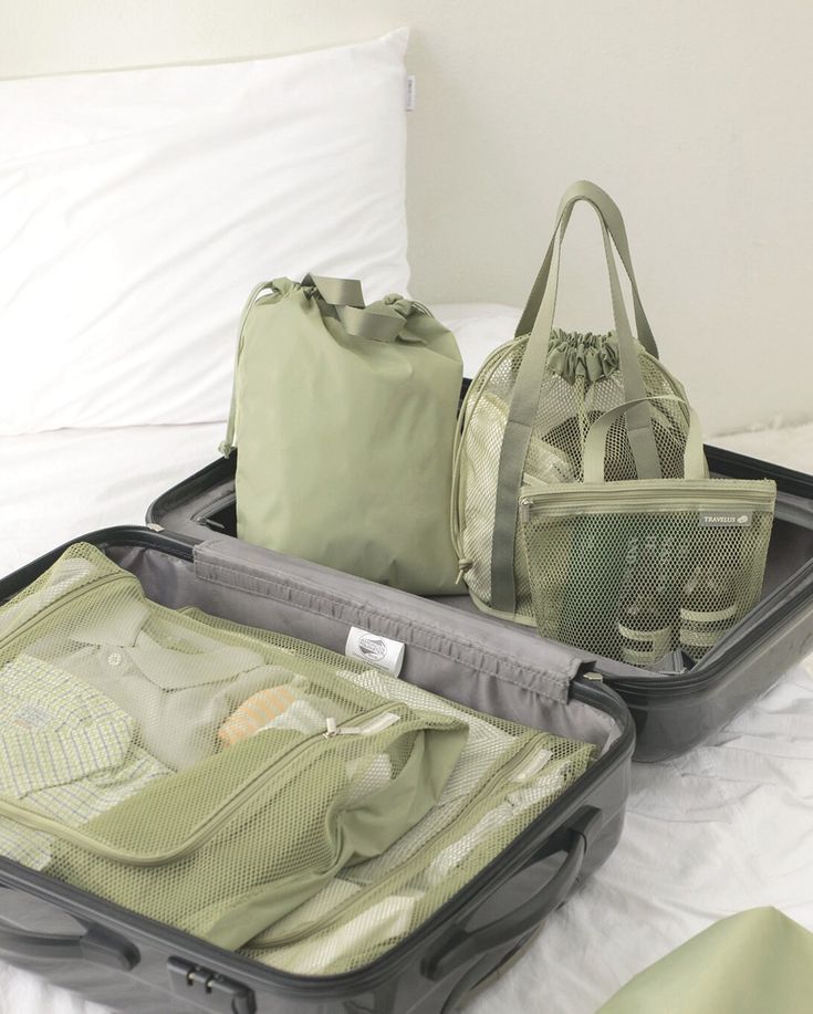 Open suitcase with neatly packed clothes in green travel organizers on a white bed. Perfect travel packing.