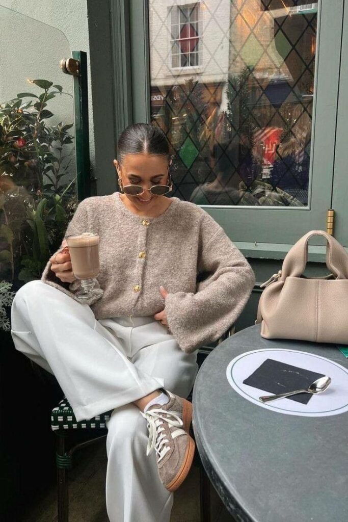 Woman in cozy sweater enjoying coffee at a stylish cafe, seated beside a table with a handbag.