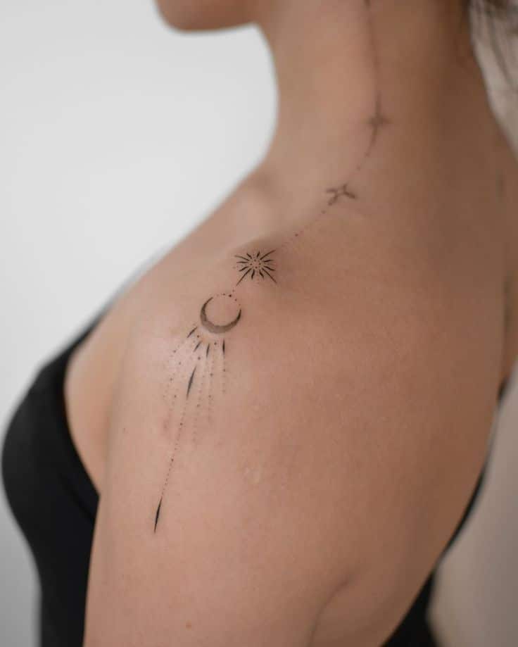 Minimalist celestial tattoo on woman's shoulder, featuring moon, stars, and dot design against neutral background. tattoo