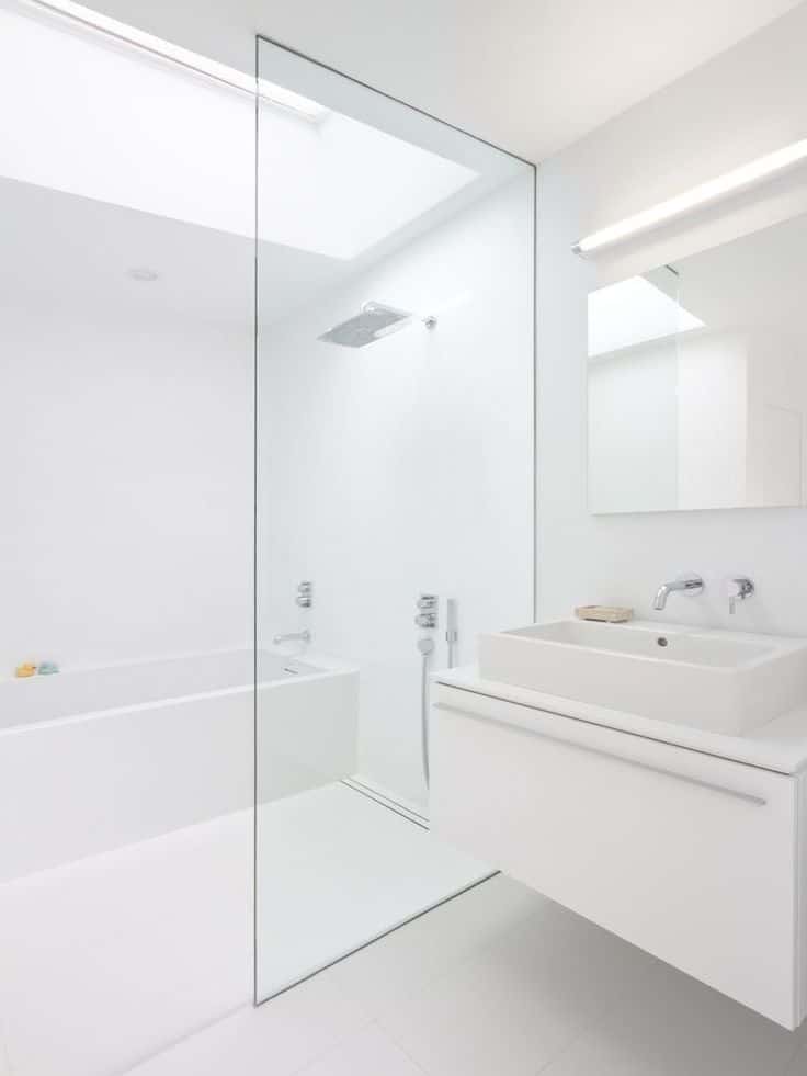 Modern white bathroom with glass shower, bathtub, and sleek vanity. Minimalist design and bright lighting.