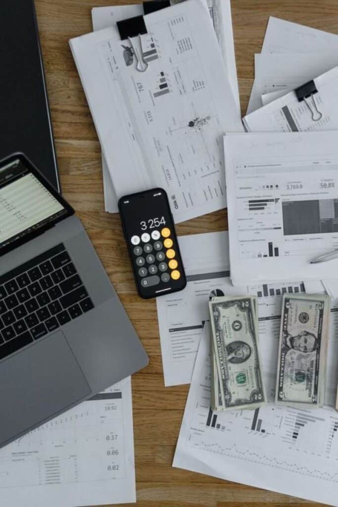 4858f3204b2344ede16c1b89ad8a0f09 Laptop, smartphone calculator, financial graphs, and dollar bills on a desk, illustrating financial analysis setup. | Sky Rye Design Laptop, smartphone calculator, financial graphs, and dollar bills on a desk, illustrating financial analysis setup.