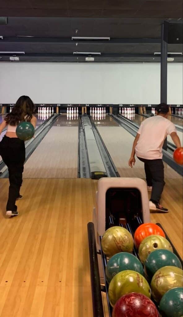 Two people bowling in a lane, focusing on rolling technique, with colorful bowling balls in the foreground.