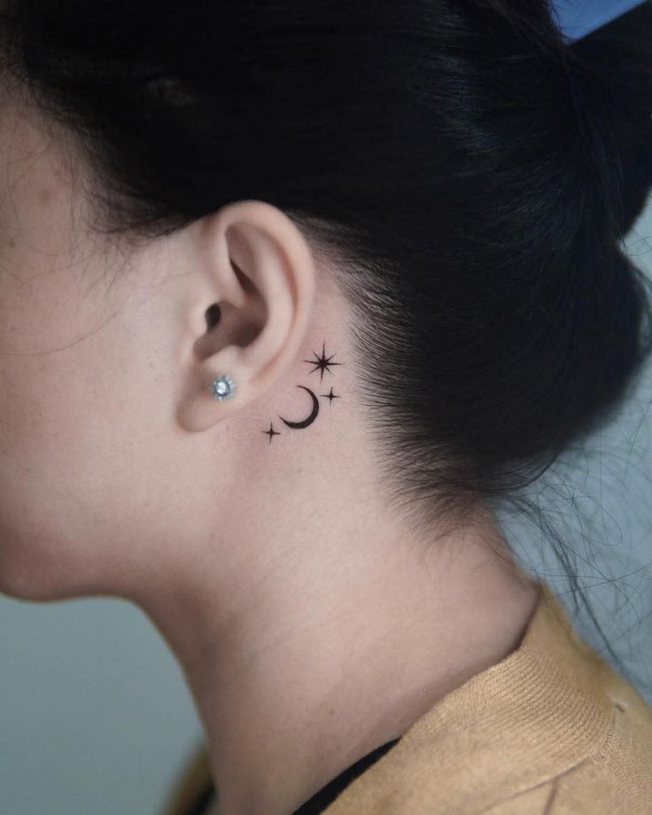Minimalist moon and stars tattoo behind ear, complemented by a diamond stud earring.
