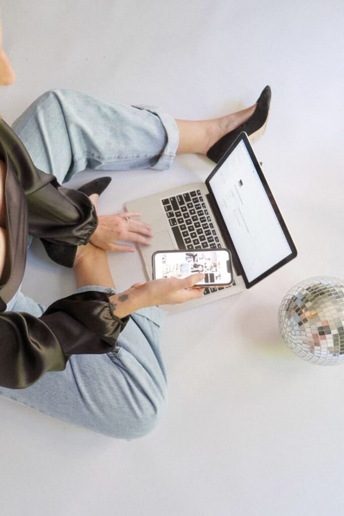 _ 5 Person using a laptop and smartphone, seated on the floor with a disco ball nearby. | Sky Rye Design Person using a laptop and smartphone, seated on the floor with a disco ball nearby.