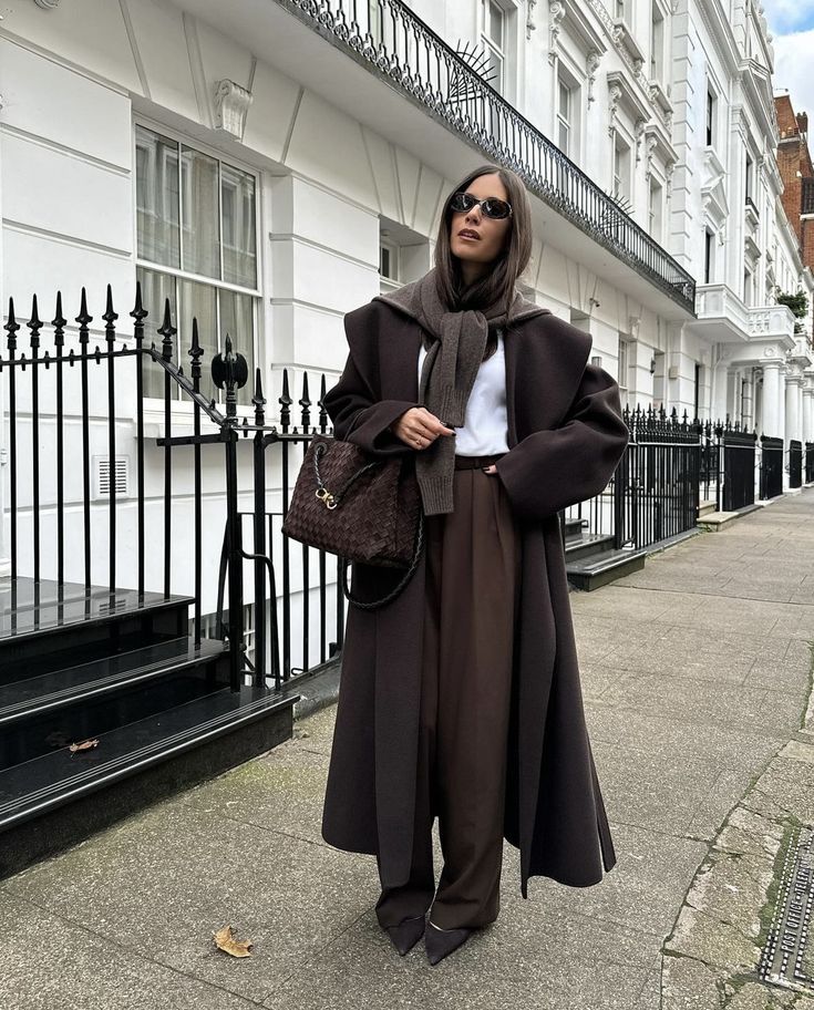 Stylish woman in brown coat and sunglasses walking in a city street, fashion look with elegance and sophistication.