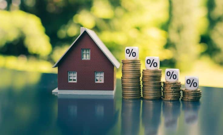 Toy house beside stacked coins with percentage signs, symbolizing mortgage interest rates and real estate investment growth.