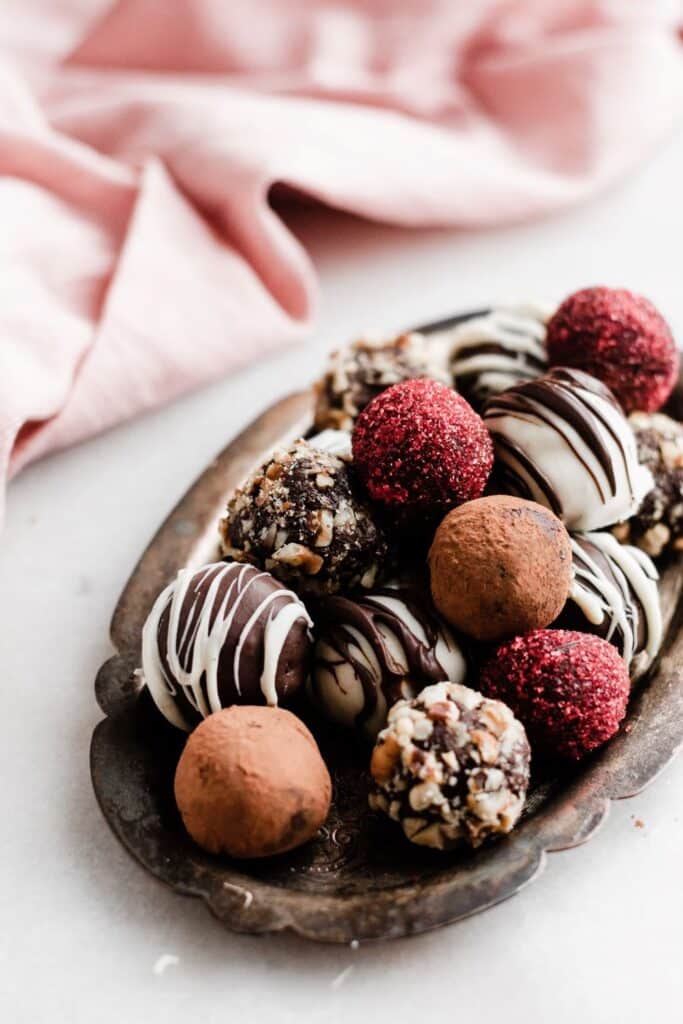 Assorted chocolate truffles arranged on a decorative silver plate with a soft pink cloth in the background.