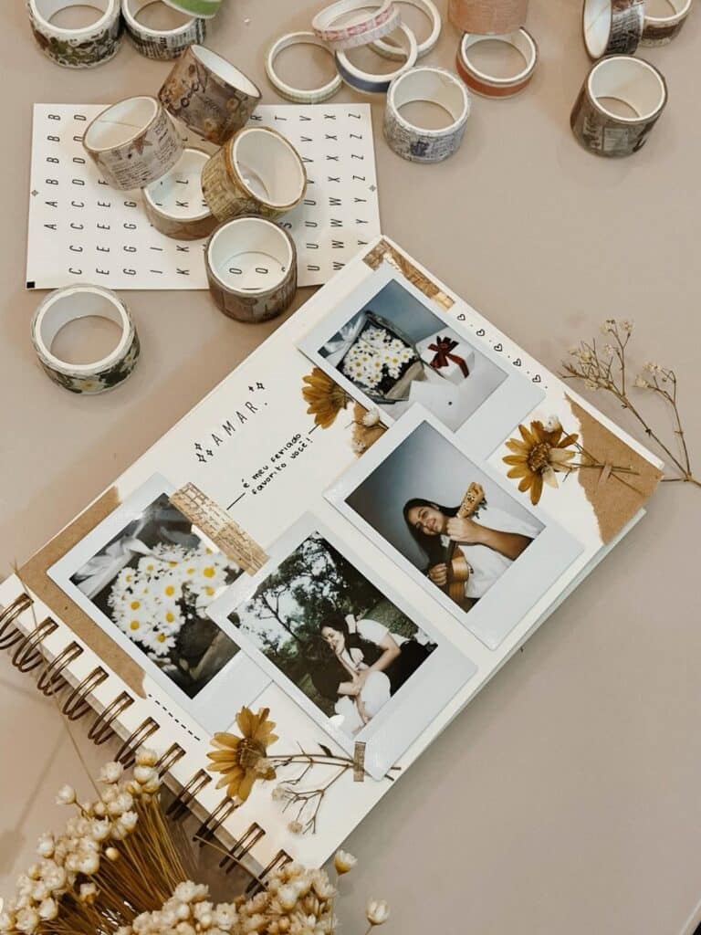 Scrapbook with Polaroid photos, decorative tape, and dried flowers on a beige background. Crafting materials scattered.