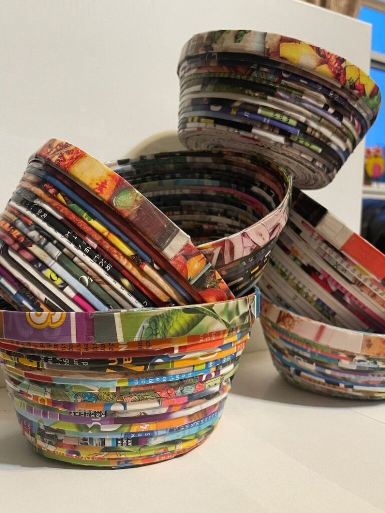 Colorful recycled magazine paper bowls stacked artistically on a white surface.