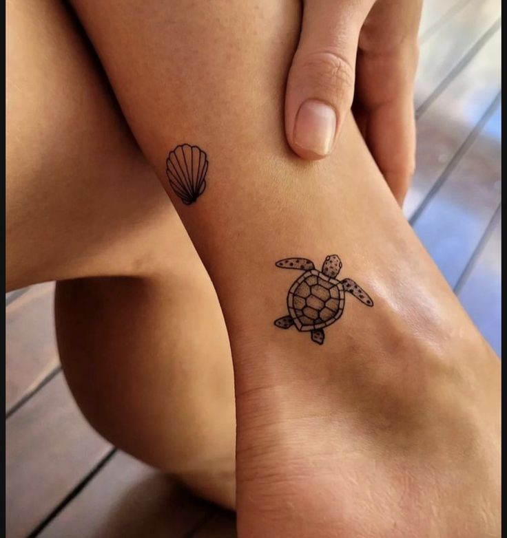 Small turtle and seashell tattoos on ankle, close-up on wooden floor background.