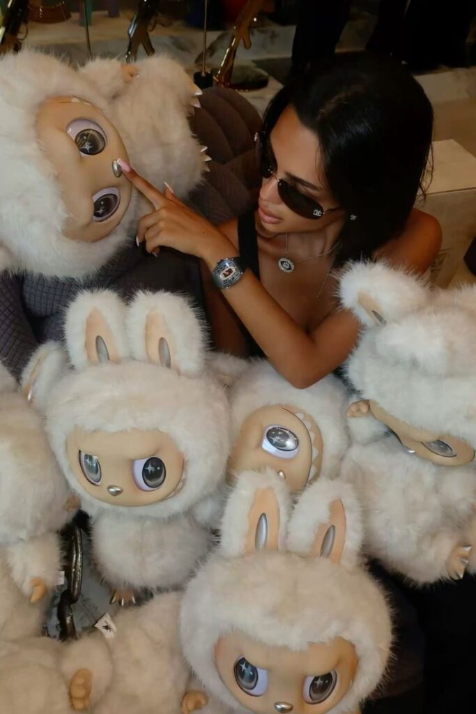 Woman in sunglasses posing with fluffy, big-eyed, white plush toys.