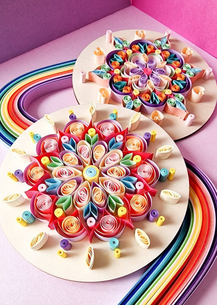 Colorful quilled paper art mandalas on wooden bases, set against pink background with rainbow strips.