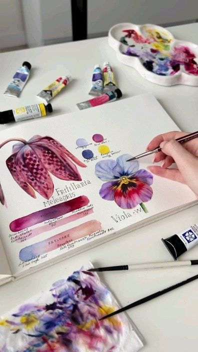 Artist painting floral watercolor sketch with vibrant hues in a sketchbook, surrounded by paint tubes and palette.