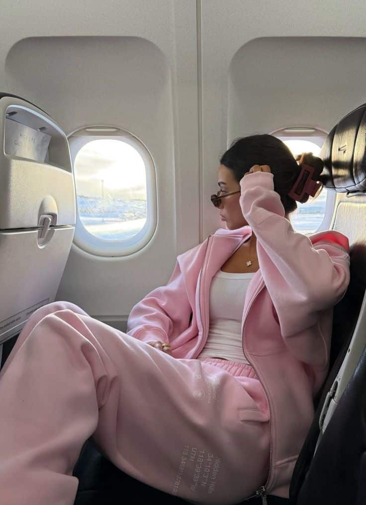 Person in a pink tracksuit relaxing and looking out an airplane window during flight.