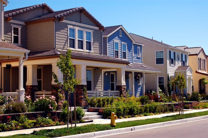 Row of modern suburban homes with gardens on a sunny day, featuring varied architectural styles and colorful facades.