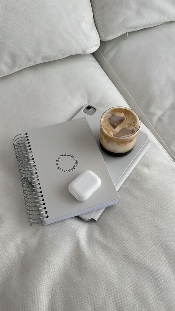 Notebook, tablet, latte, and earbuds on a white sofa, creating a cozy and productive workspace atmosphere.