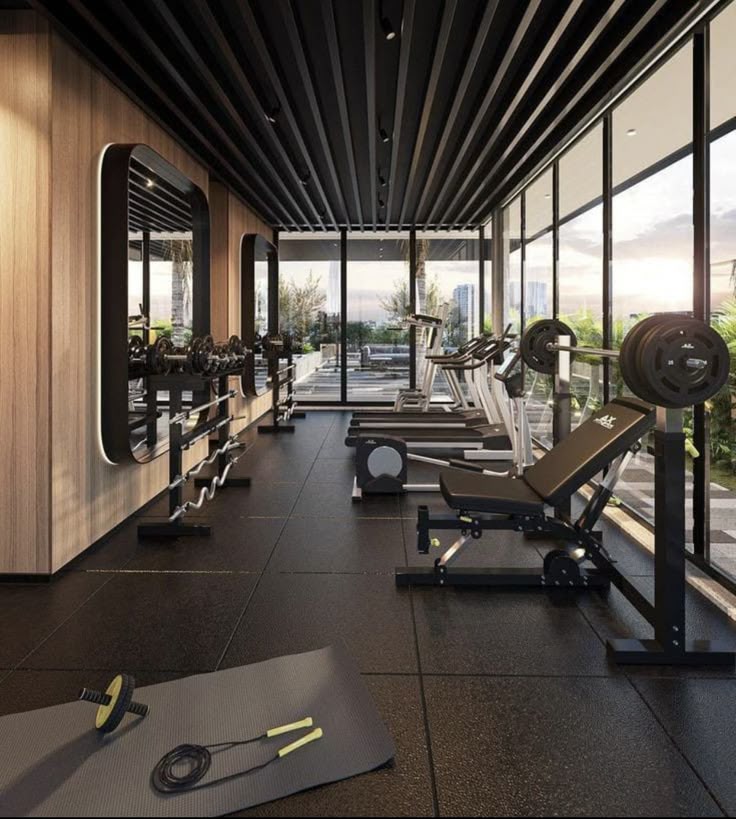 Modern gym with weight bench, exercise mats, and cardio machines by a window with city view.