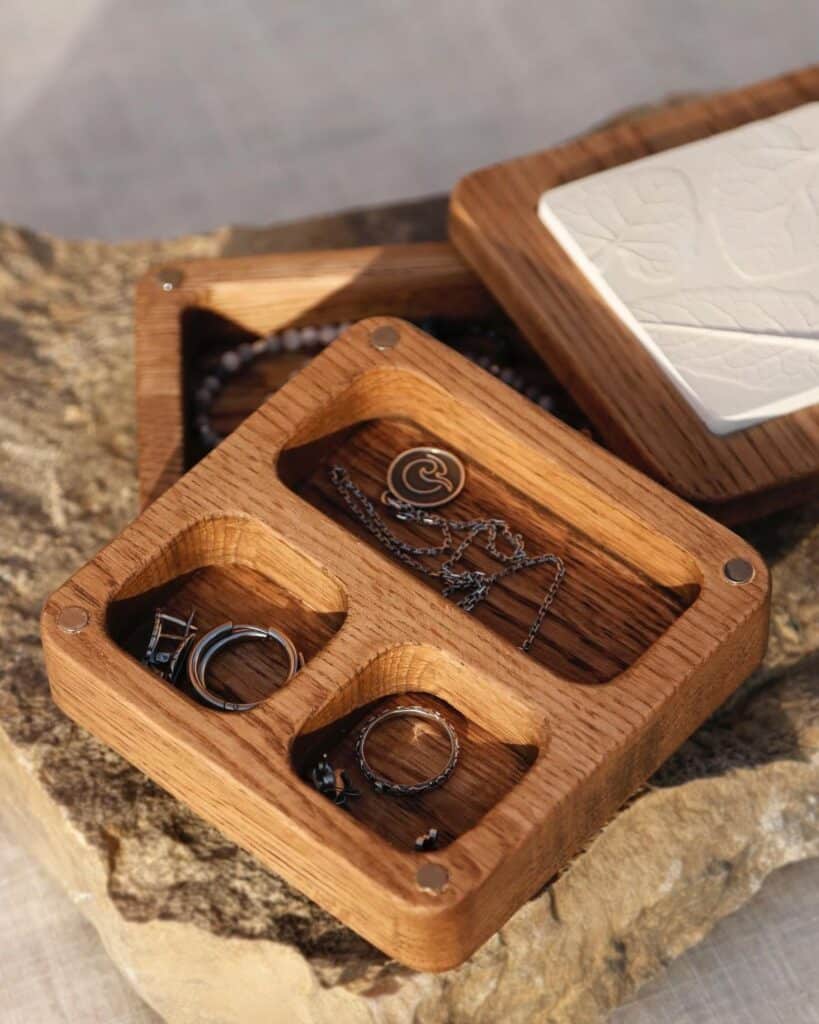Wooden jewelry organizer with compartments holding rings and chains on a stone surface. Stylish and functional storage.