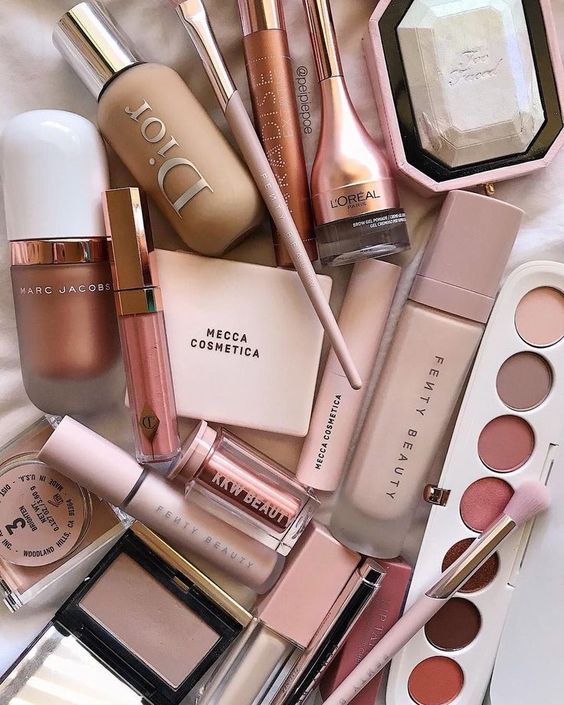 Variety of beauty products from luxury brands, including makeup palettes, foundations, and lipsticks, in pink and nude hues.