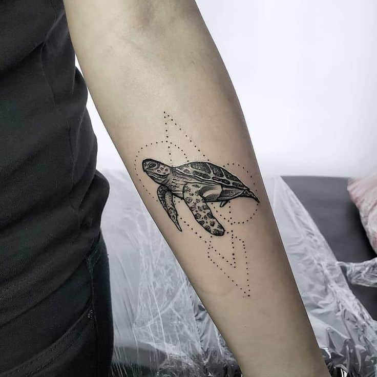 Forearm tattoo of a black and grey sea turtle with geometric dot design.